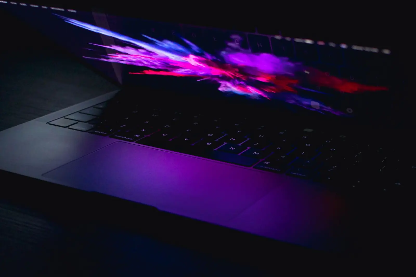 A laptop in the dark, its half-open screen glowing pink and violet